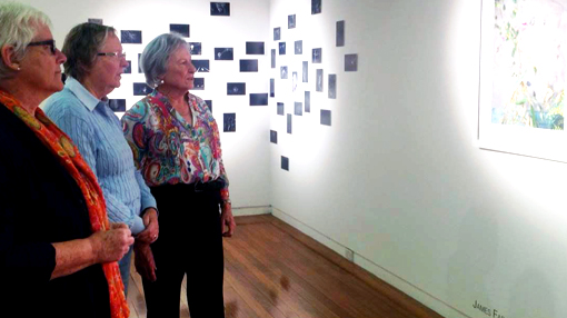 three women stand in a gallery looking at a painting on the wall