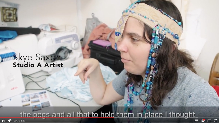 Screenshot from the film: Skye Saxon, wearing a hand made head piece, discusses her work
