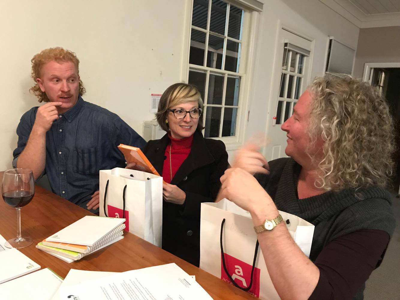 Luke, Sue and Darlene sit together at a table, interacting, holding Accessilbe Arts bags
