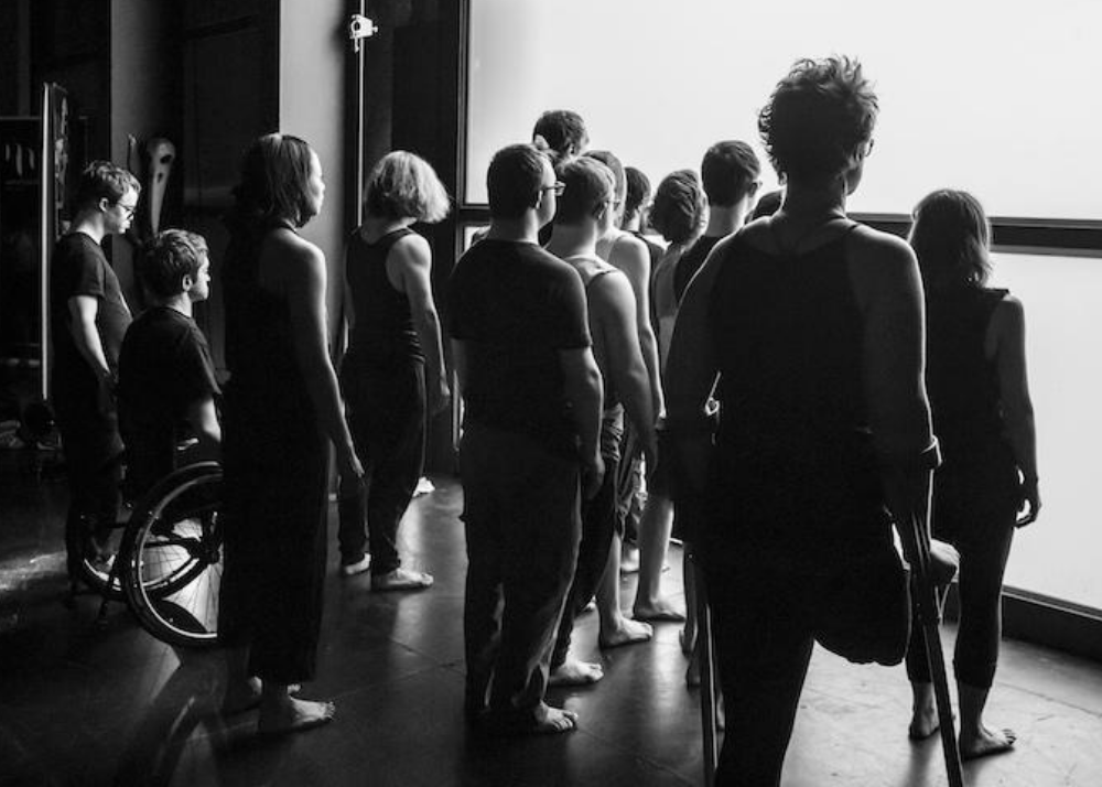 a group of people of various ages and genders lined up in front of a glowing white screen