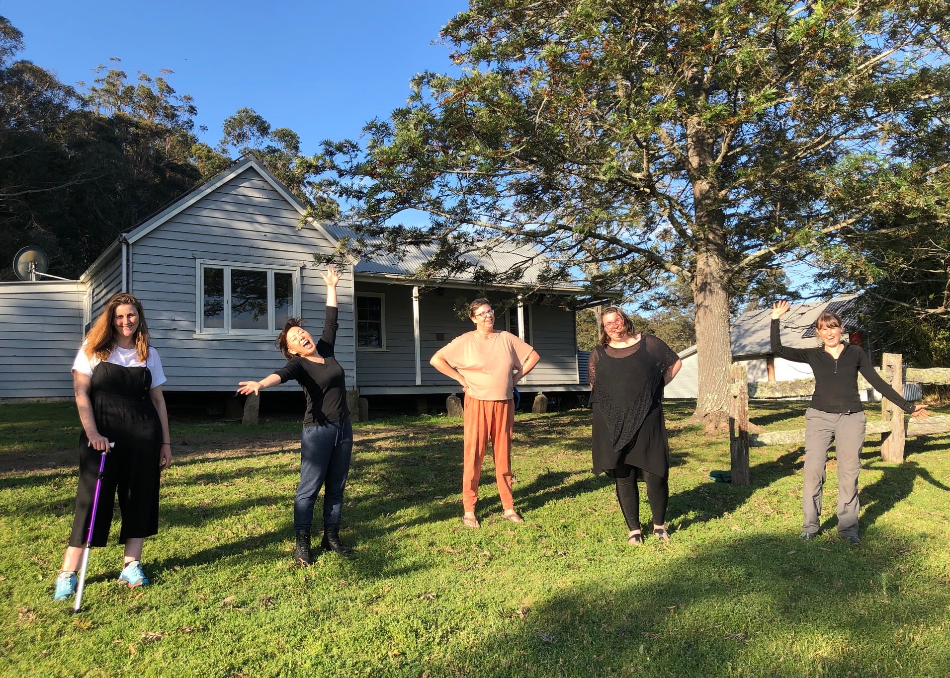 Five women of various ages and cultural backgrounds standing in front of a cabin in the bush.